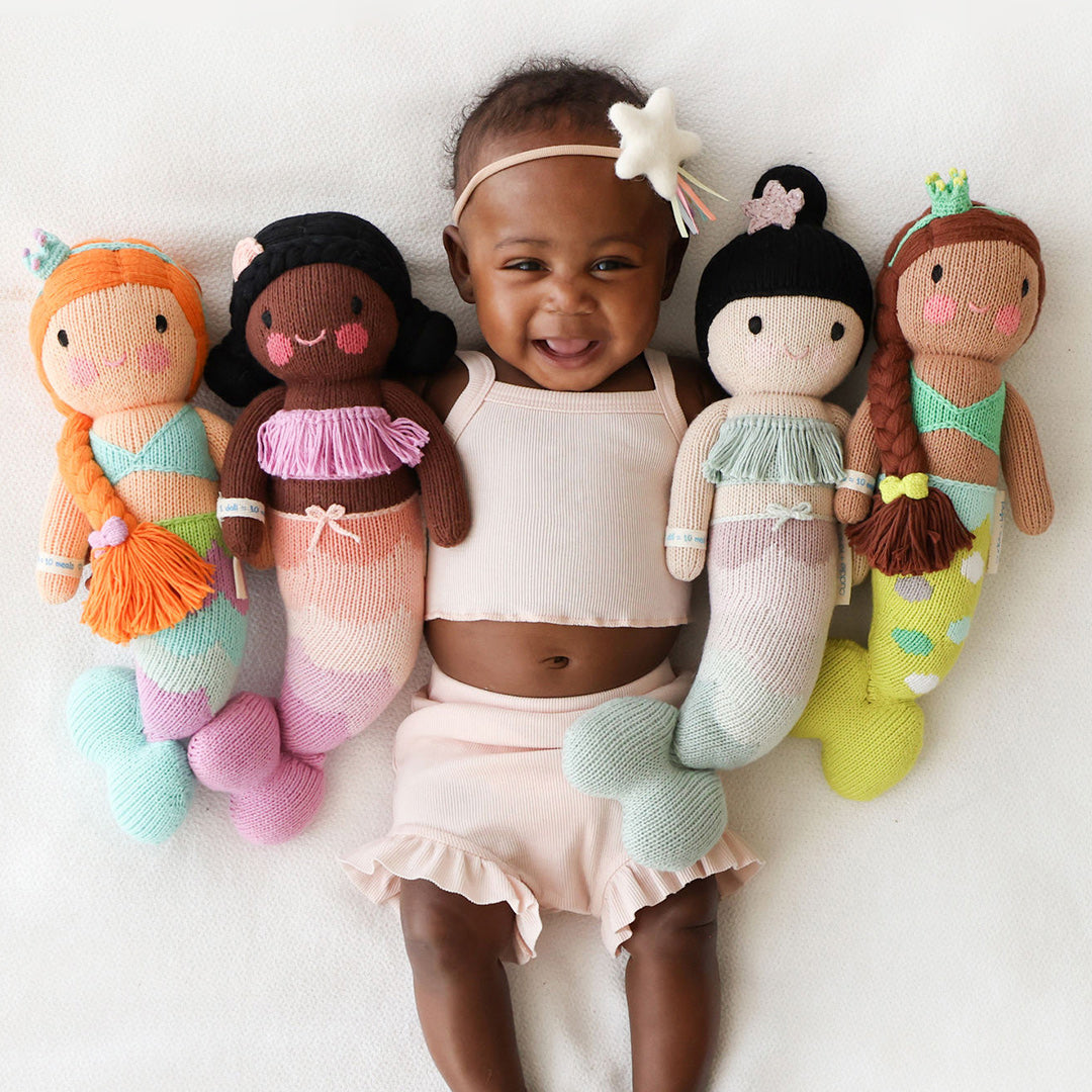 A baby holding four mermaid stuffed dolls: Isla, Maya, Luna and Pearl