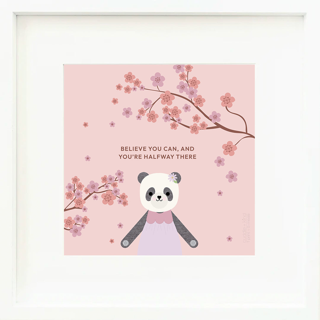An inspirational print with a graphic of Polly the panda between the limbs of a flowering cherry tree on a pink background with the words “Believe you can, and you’re halfway there” in currant.