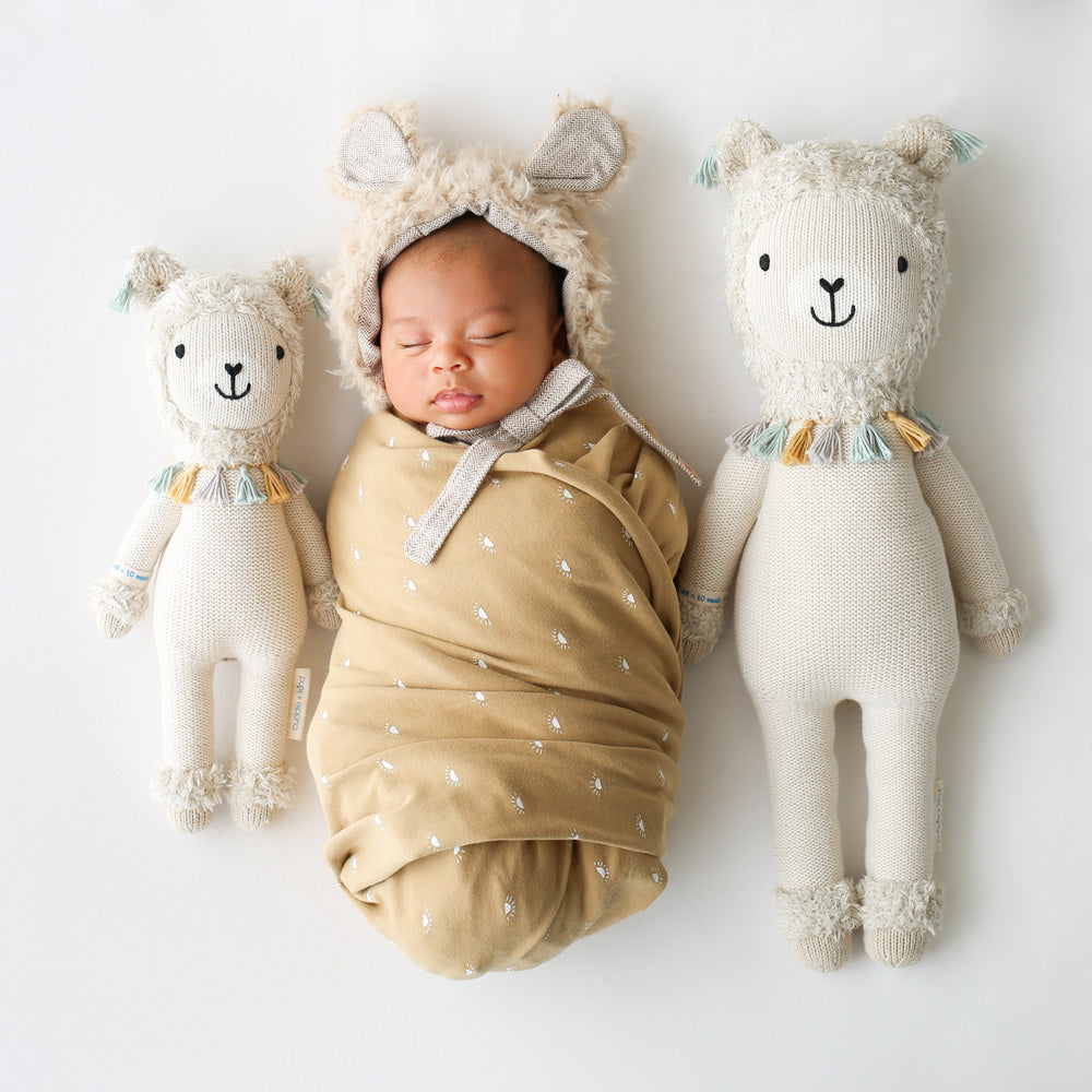 A sleeping baby snuggled between two Lucas the llama stuffed dolls in the little and regular sizes.